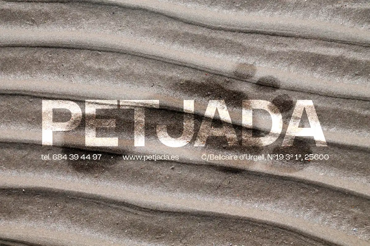 Arena mojada con una huella y el logo de PETJADA en el centro.
